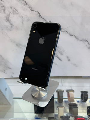 A black Apple iPhone 8 displayed on a silver stand, showing the back of the phone with the Apple logo and 'iPhone' text, set against a white marble-patterned background.