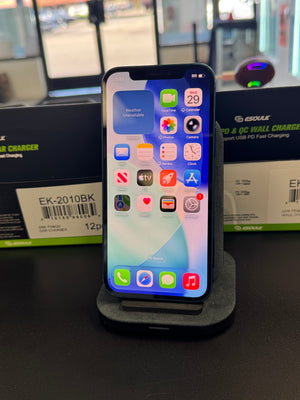 A black smartphone with its screen on, resting on a matching black charging stand. The background shows two black and green boxes for an 'ESQULK' 12W fast charger on a dark table.