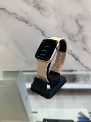 A smartwatch with a light beige band and a gold-toned case, displayed on a black stand against a white marble-patterned background.