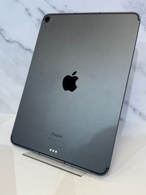A dark gray Apple iPad Air shown from the back, resting on a clear acrylic stand against a white marble-patterned background.