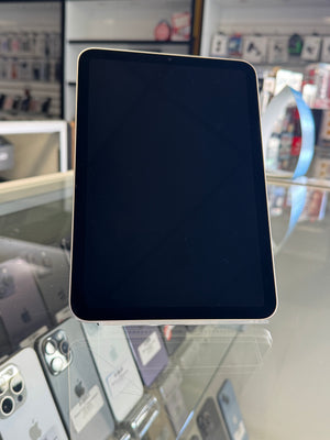 A black tablet with a silver bumper frame displayed on a glass counter inside a retail store, with other phones and store fixtures blurred in the background.