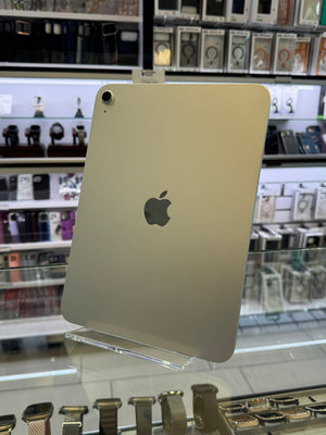 An Apple iPad with a light aluminum back and the iconic black Apple logo, displayed on a clear stand inside a retail store.