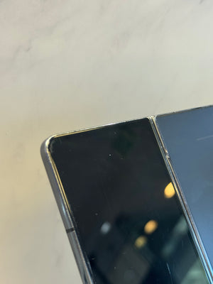 Close-up of a black foldable smartphone showing the hinge and outer screen edge against a light marble-like background.