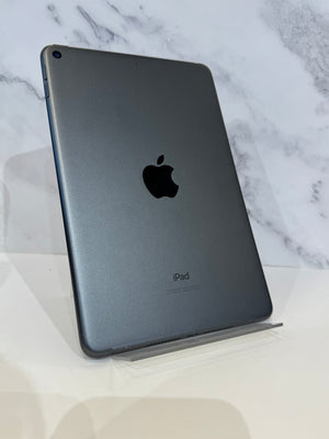 A dark gray Apple iPad shown from the back, standing upright on a clear acrylic display stand against a white marble-patterned background.