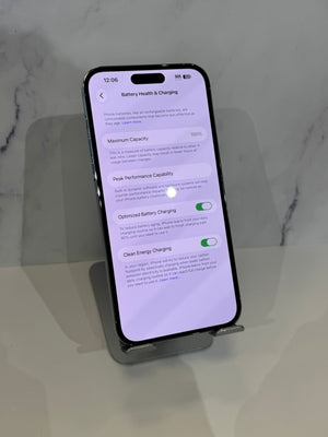 A black smartphone displayed upright on a small stand, showing the Battery Health & Charging settings screen on a light gray marble-like surface.