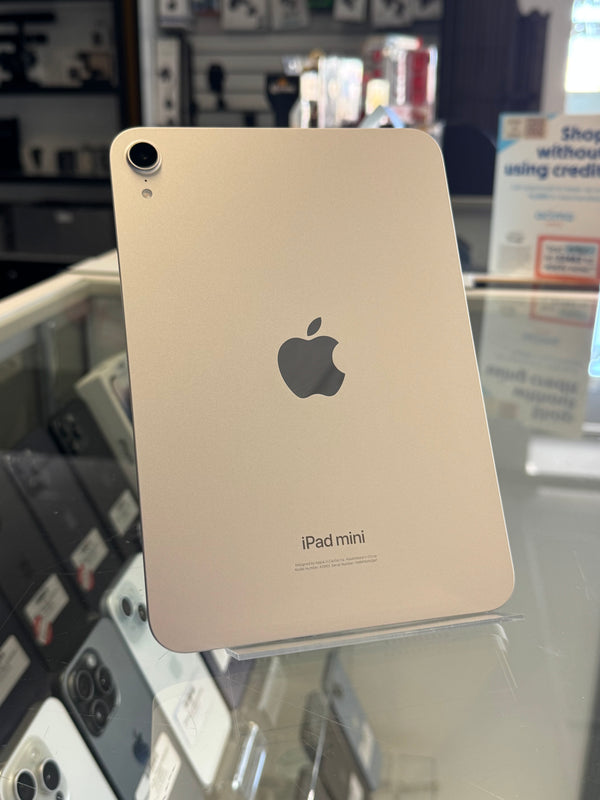 An Apple iPad mini is displayed on a stand inside a retail store, showing its back with the Apple logo and 'iPad mini' text.