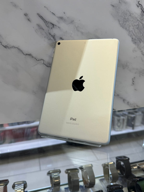 An Apple iPad with a light gold back panel and a blue edge, displayed on a stand in front of a white marble-patterned background.