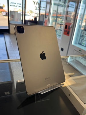 An Apple iPad Pro standing upright on a clear display stand inside a retail store, showing the back of the device with the Apple logo and camera module visible.