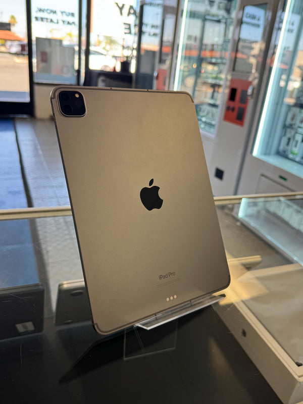 An Apple iPad Pro standing upright on a clear display stand inside a retail store, showing the back of the device with the Apple logo and camera module visible.