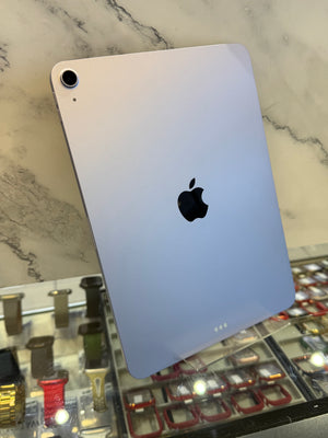 A silver Apple iPad shown from the back, leaning on a glass display case against a white marble-patterned background.