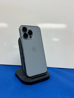 A gray Apple iPhone Pro showing the back of the device, resting on a black charging stand against a white background with a blue surface below.