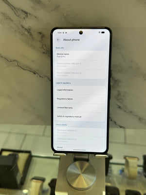A black smartphone displaying the 'About phone' settings page on its screen, resting on a metallic display stand in front of a marble-patterned wall.