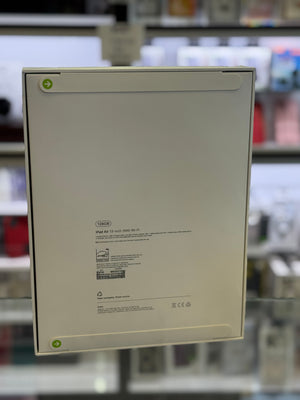 The back of a white Apple iPad Air packaging box, showing product specifications and barcodes, photographed in a blurred retail store setting.