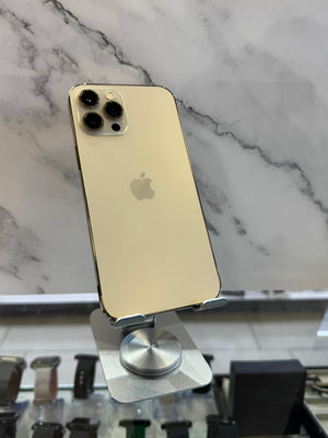 A gold Apple iPhone 12 Pro displayed on a silver stand, showing its back panel with the Apple logo, set against a white marble background.