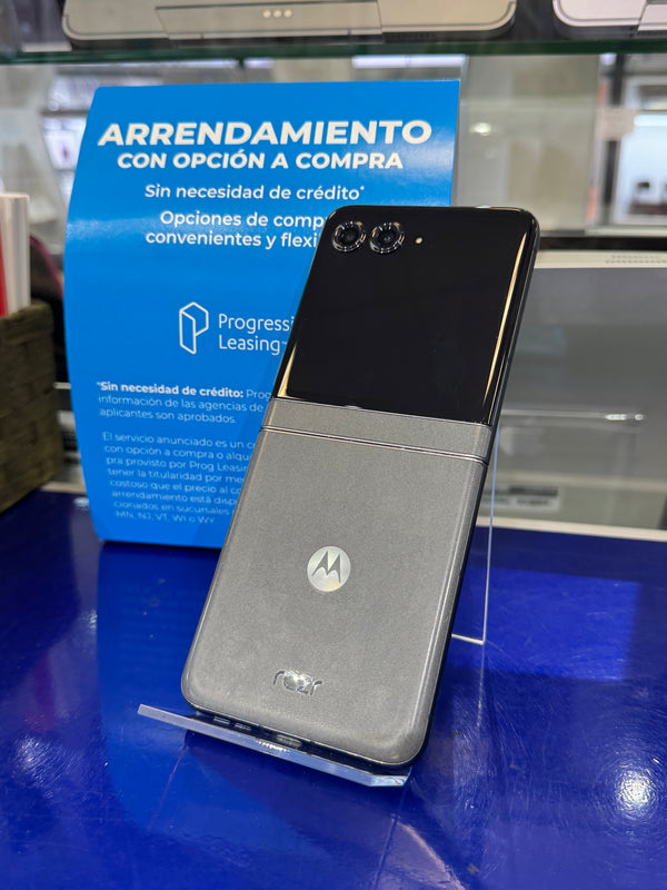 A silver and black Motorola flip phone shown open, resting on a blue promotional display stand in a retail setting.