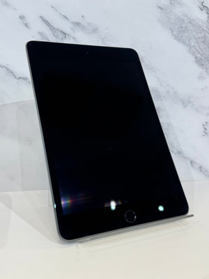 A black tablet device with rounded corners and a home button, displayed upright on a clear stand against a white marble-patterned background.
