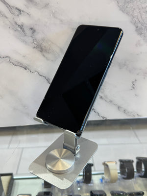 A black smartphone displayed on a silver metal stand, set against a white marble-patterned background.