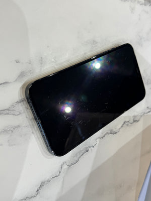 A black smartphone with a glossy screen lying on a white marble-patterned surface.
