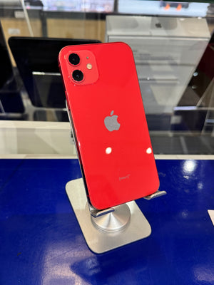 A red Apple iPhone shown from the back, resting on a silver display stand on a blue counter in a store setting.