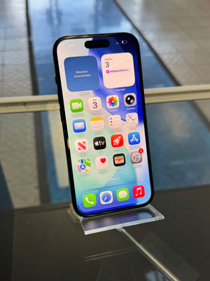 Apple smartphone with the screen displaying various apps standing upright on a clear acrylic stand on a glass shelf