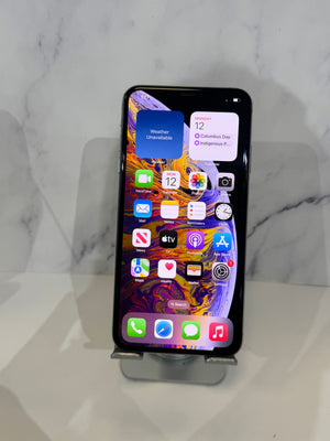 A black Apple iPhone with its screen on, resting on a clear phone stand against a white marble-patterned background.