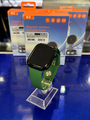 Green smartwatch on a clear stand with K3 magnetic wireless charging stand packaging in the background.