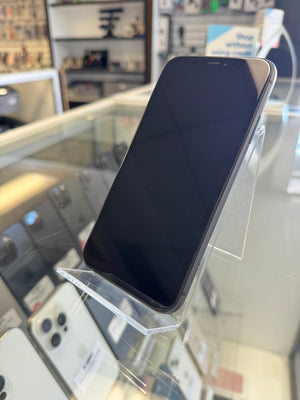 A black smartphone with a blank screen, displayed on a clear acrylic stand inside a retail store.