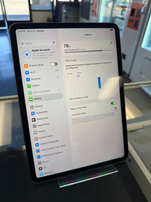 A black tablet displaying the Settings app battery page, standing on a small display stand in a retail or office environment.