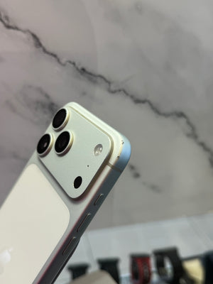 A close-up of the rear corner of an iPhone showing its light gold back, triple rear camera array, and a light blue front bumper edge, set against a gray marble-patterned background.