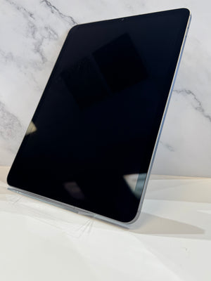 A silver tablet with a black screen, standing upright on a white surface against a white marble-patterned background.