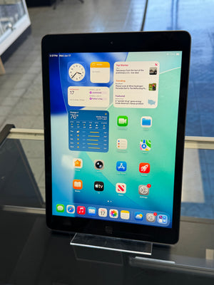 Tablet device displaying a home screen with various app icons on a reflective surface.