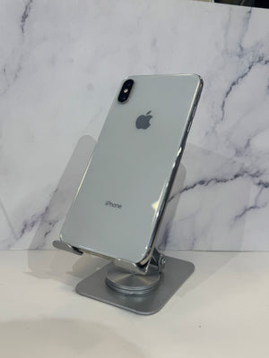 A silver Apple iPhone X showing the back of the device, resting on a metallic stand against a white marble-patterned background.