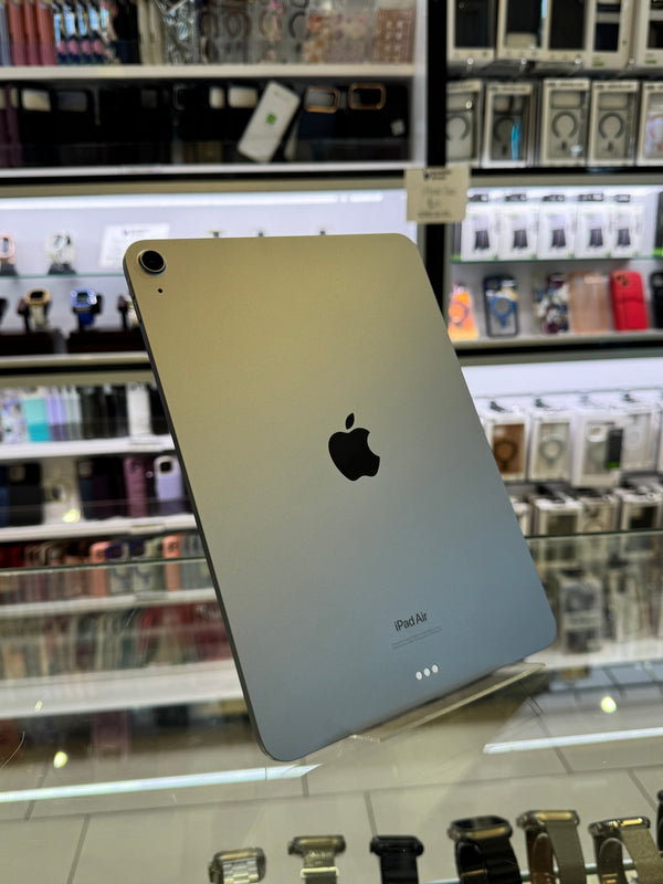 An Apple iPad Pro shown from the back, resting on a glass display counter inside a retail store. The device has a metallic silver finish with the black Apple logo in the center.