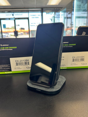 A black smartphone displayed on a gray and black wireless charging dock, set against its product packaging box on a dark tabletop.
