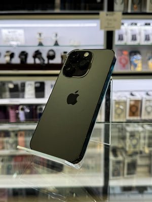 A dark green Apple iPhone Pro showing its back side with the Apple logo, displayed on a clear stand inside a retail store.