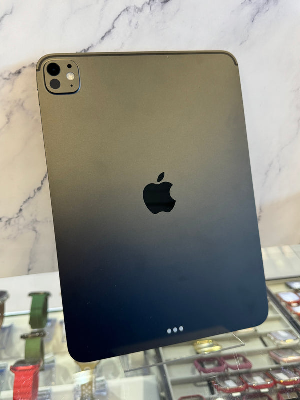 A dark gray Apple iPad shown from the back, standing upright on a display stand in front of a white marble-patterned wall.