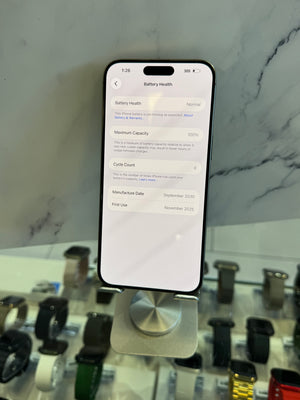 A black smartphone displaying the battery health settings screen, resting on a white marble-like surface with a blurred watch display case in the background.