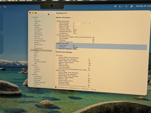 A close-up of a computer screen showing the macOS System Preferences interface, with the Apple logo and a MacBook Pro battery information panel visible.