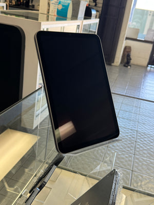 A black tablet with a glossy screen, likely an iPad, displayed on a clear acrylic stand inside a retail store.