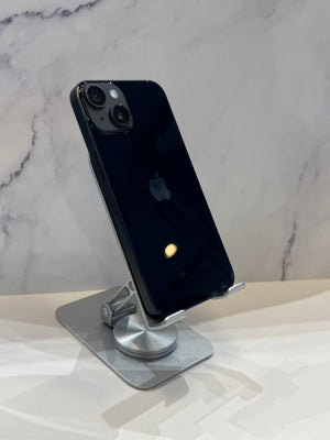 A black Apple iPhone shown from the back, resting on a silver metal stand against a light marble-patterned background.