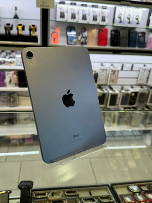 A silver Apple iPhone shown from the back, resting on a glass display case inside a retail store with shelves of phone accessories in the background.