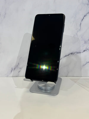 A black smartphone displayed upright on a silver metal stand against a white marble-patterned background.