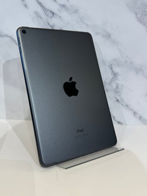A dark gray Apple iPad shown from the back, standing upright on a clear acrylic display stand against a white marble-patterned background.