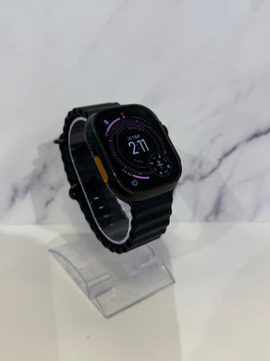A black smartwatch with a black strap and a digital display showing the time 2:11, resting on a clear plastic display stand against a white marble-patterned background.