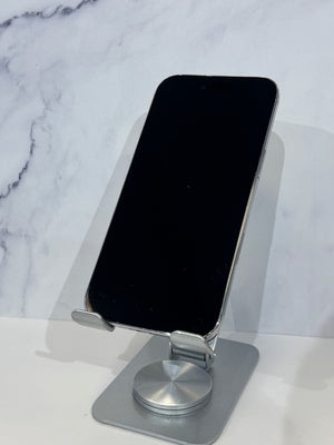 A silver metal phone stand holding a black smartphone, set against a white marble-patterned background.