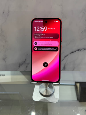 A red iPhone with a black front and a pink and purple wallpaper, resting on a silver metal stand on a glass table. The background features a gray marble-patterned wall.