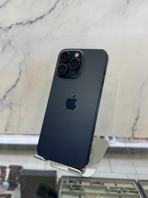 A dark blue Apple iPhone Pro showing the back of the device with its triple-camera system and Apple logo, displayed on a stand in front of a marble-patterned background.