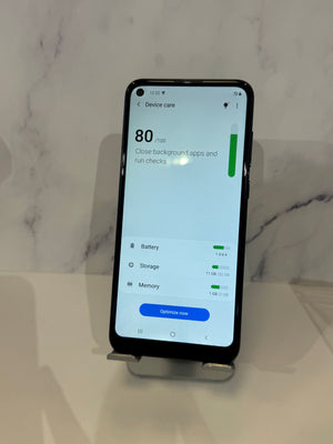 A black smartphone displayed upright on a small stand against a light marble-patterned background, with the screen showing a device care app interface.