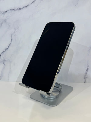 A silver metal phone stand holding a black smartphone, set against a white marble-patterned background.