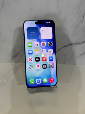 A black iPhone with its screen turned on and displaying the home screen, resting on a small metal display stand against a light gray marble-patterned background.